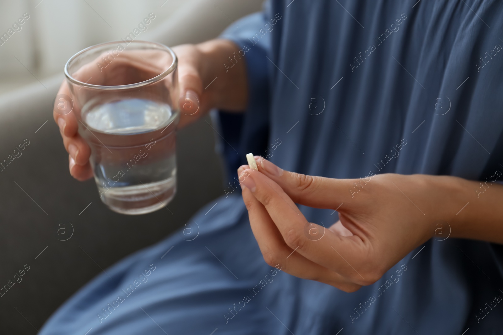 Photo of Woman with glass of water taking pill at home, closeup