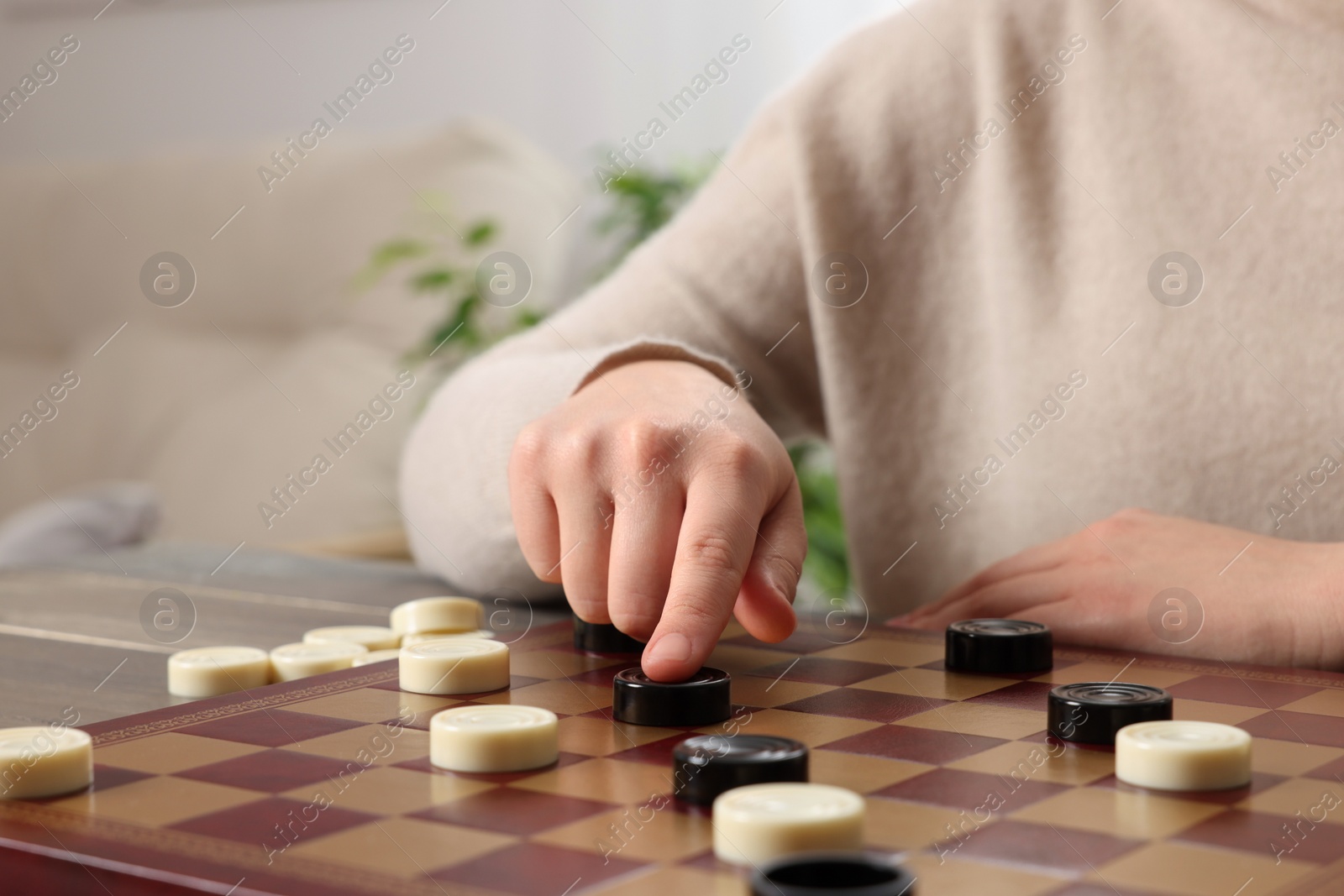 Photo of Playing checkers. Woman thinking about next move at table in room, closeup