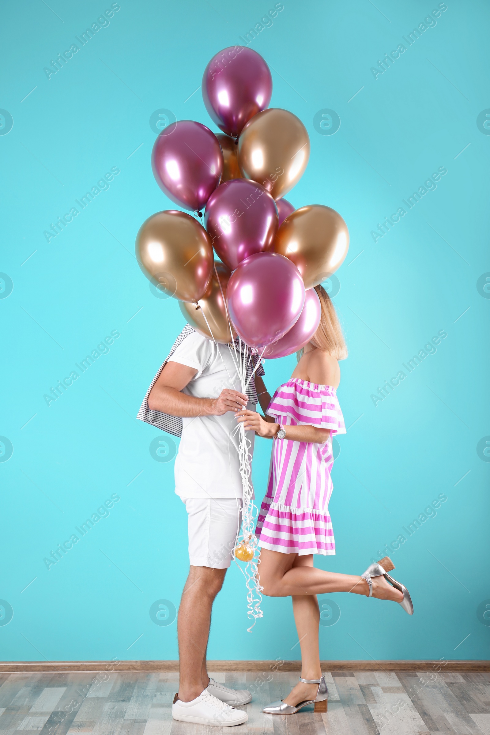 Photo of Young couple hiding behind air balloons near color wall