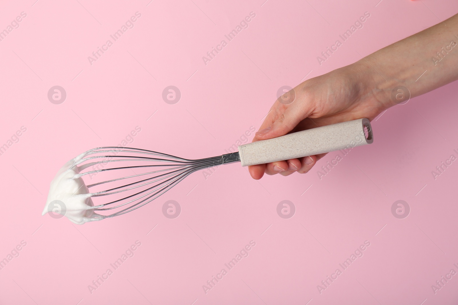 Photo of Woman holding whisk with whipped cream on pink background, closeup