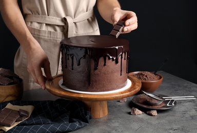 Photo of Chef making fresh delicious chocolate cake at grey table, closeup