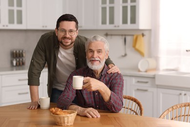 Happy son and his dad at wooden table in kitchen