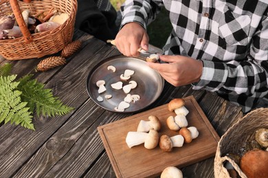 Photo of Man cutting fresh mushrooms with knife at wooden table outdoors, closeup