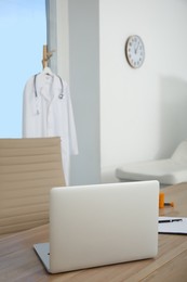 Photo of Modern laptop on wooden table in medical office. Interior design