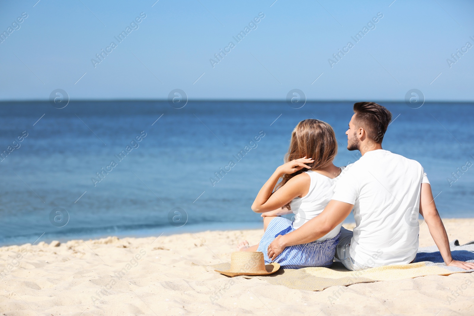 Photo of Happy young couple sitting together at beach on sunny day