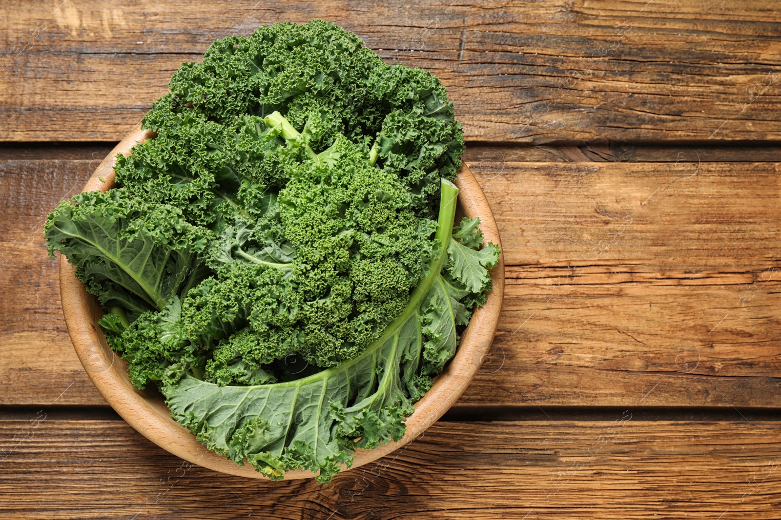 Photo of Fresh kale leaves on wooden table, top view. Space for text