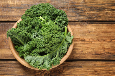 Photo of Fresh kale leaves on wooden table, top view. Space for text