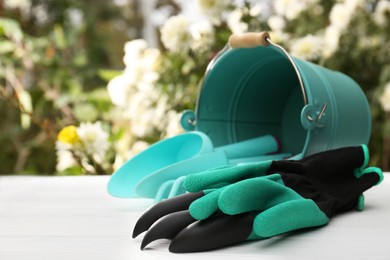 Photo of Gardening gloves and overturned bucket with different tools on white wooden table outdoors, space for text