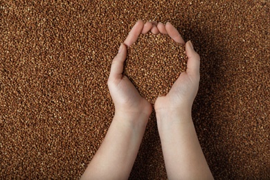 Closeup of woman holding raw buckwheat over grains, top view. Space for text