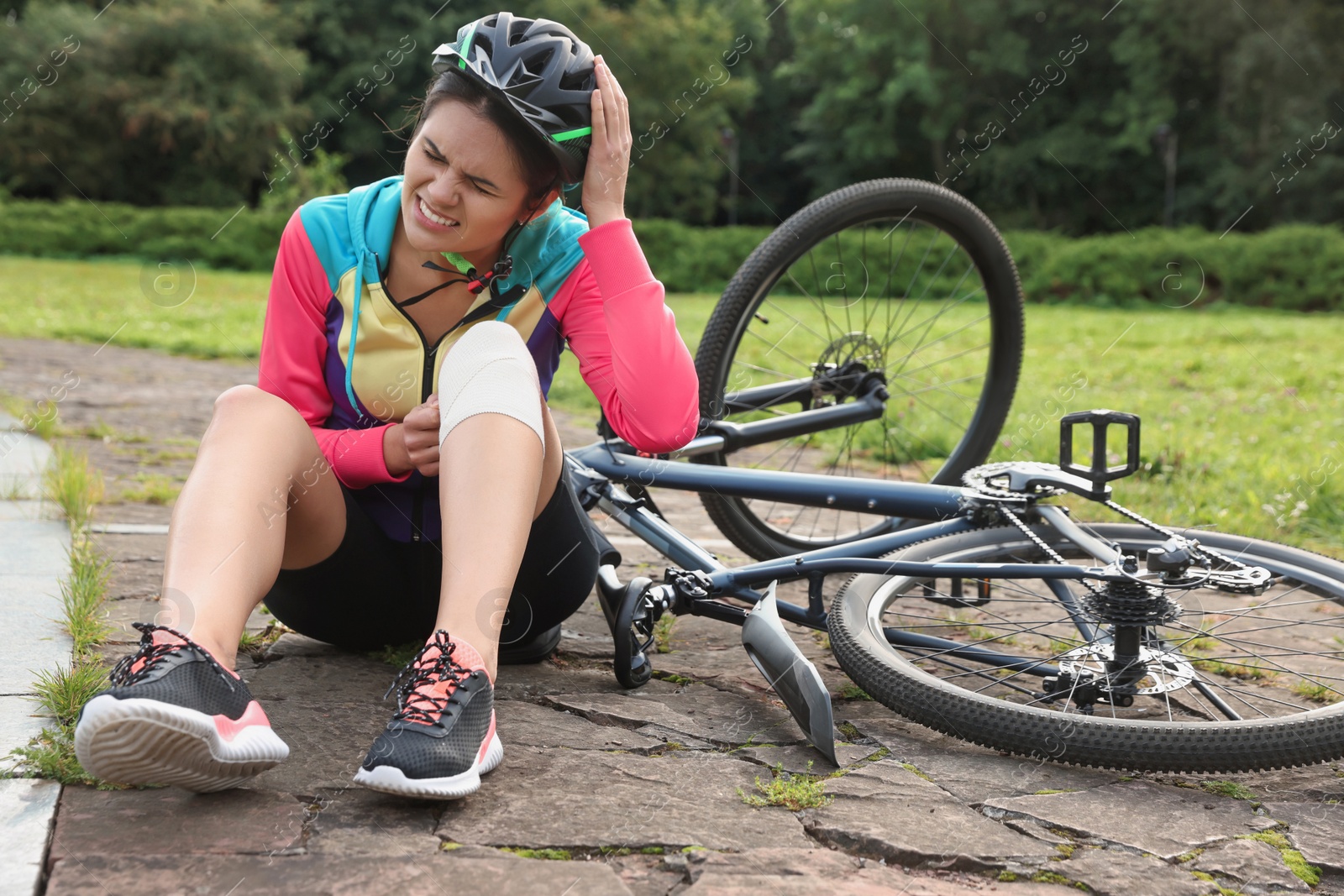 Photo of Young woman with injured knee near bicycle outdoors