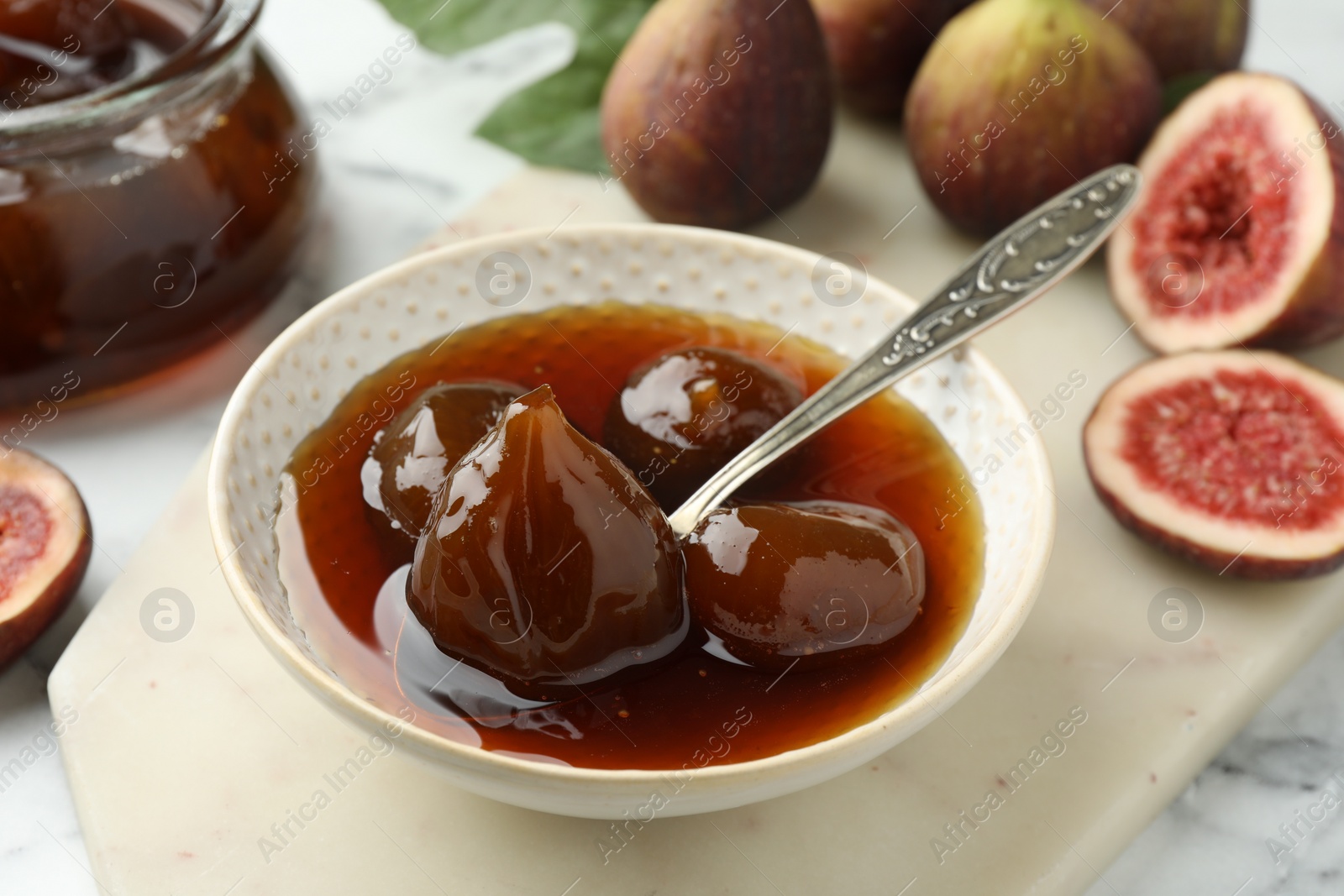 Photo of Bowl of tasty sweet jam and fresh figs on white marble table