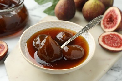 Photo of Bowl of tasty sweet jam and fresh figs on white marble table