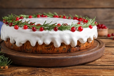 Photo of Traditional Christmas cake decorated with rosemary and cranberries on wooden table, closeup