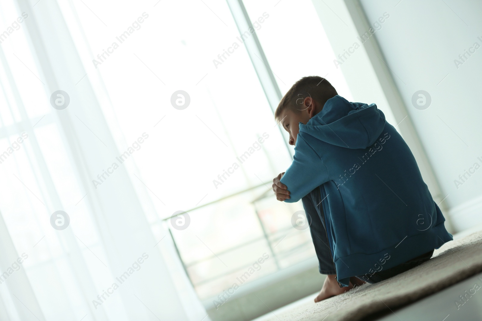 Photo of Upset boy sitting near window indoors. Space for text