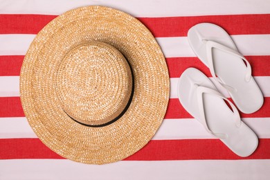 Photo of Hat and flip flops on striped beach towel, flat lay