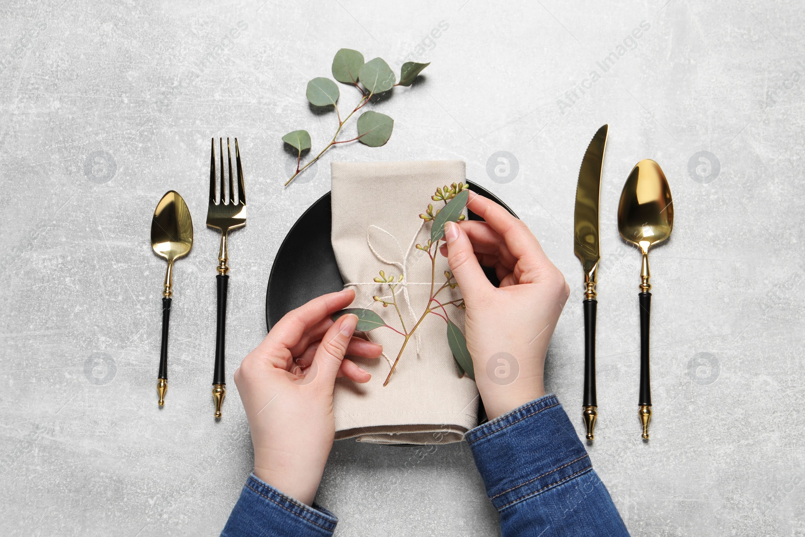 Photo of Woman decorating table setting with eucalyptus leaves, top view