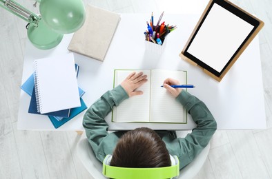 Photo of Cute little boy with modern tablet studying online at home, top view. E-learning