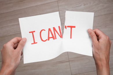 Photo of Motivation concept. Woman making phrase I Can from I Can't by tearing paper indoors, closeup