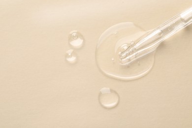 Glass pipette and transparent liquid on beige background, top view. Space for text