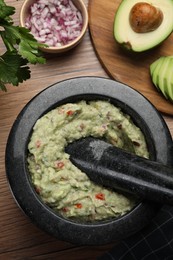 Photo of Delicious guacamole in mortar and ingredients on wooden table, flat lay