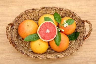Photo of Wicker basket with fresh ripe grapefruits and green leaves on wooden table, top view