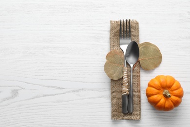Photo of Cutlery with leaves, pumpkin and space for text on white wooden background, flat lay. Table setting elements