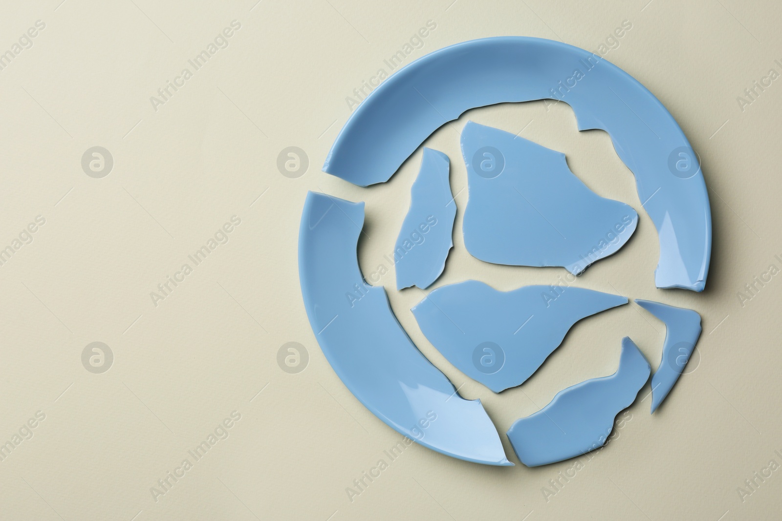 Photo of Pieces of broken ceramic plate on beige background, top view. Space for text