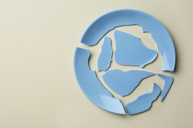 Pieces of broken ceramic plate on beige background, top view. Space for text