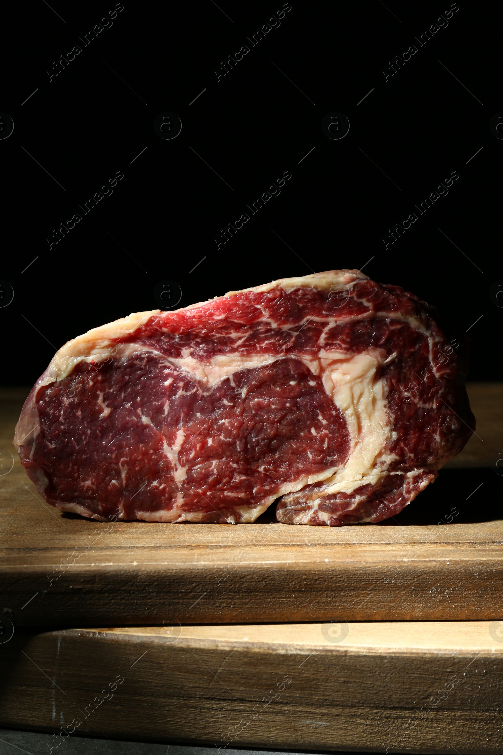 Photo of Piece of raw beef meat on wooden board against black background, closeup