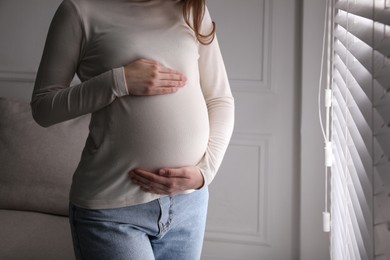 Photo of Young pregnant woman near window at home, closeup. Space for text