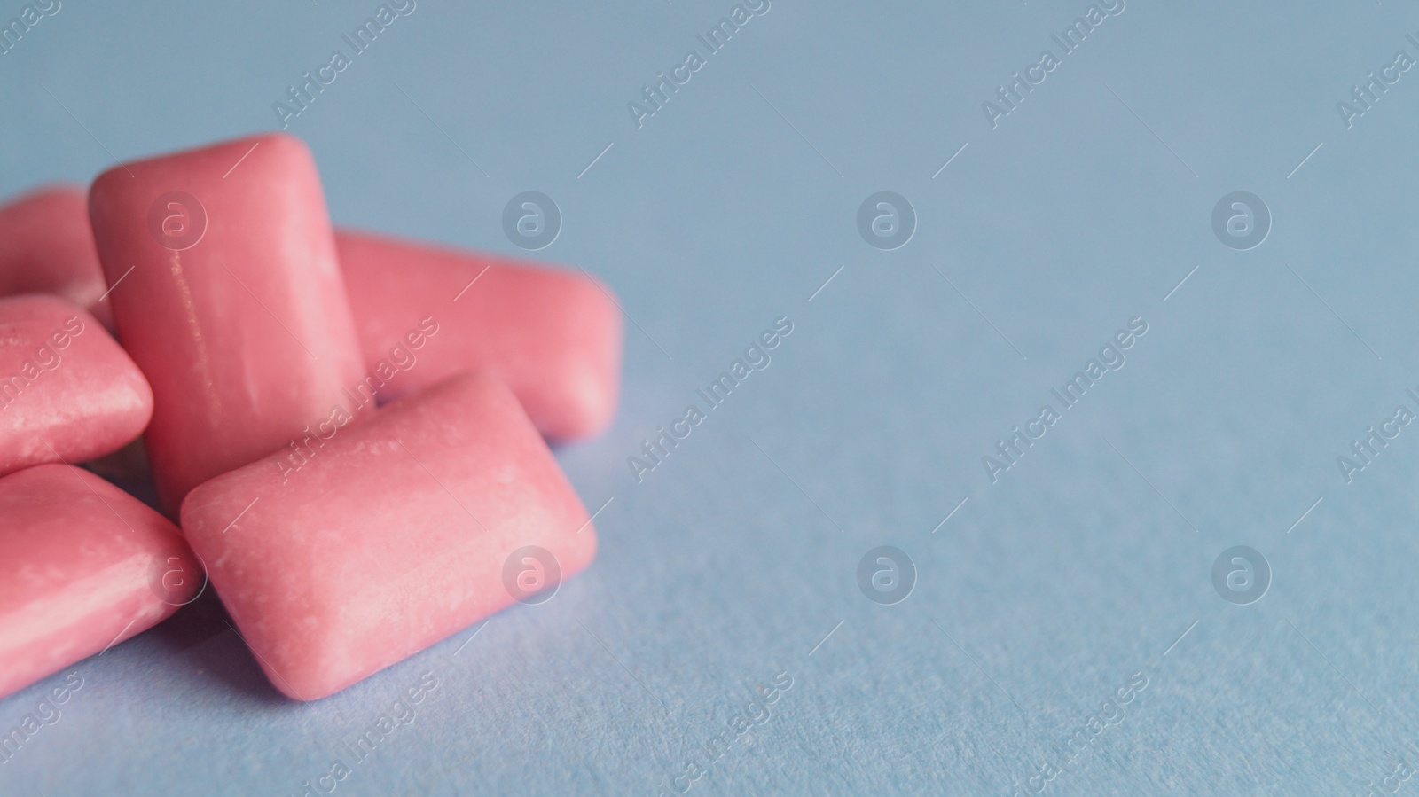 Photo of Heap of sweet chewing gums on light blue background, closeup. Space for text