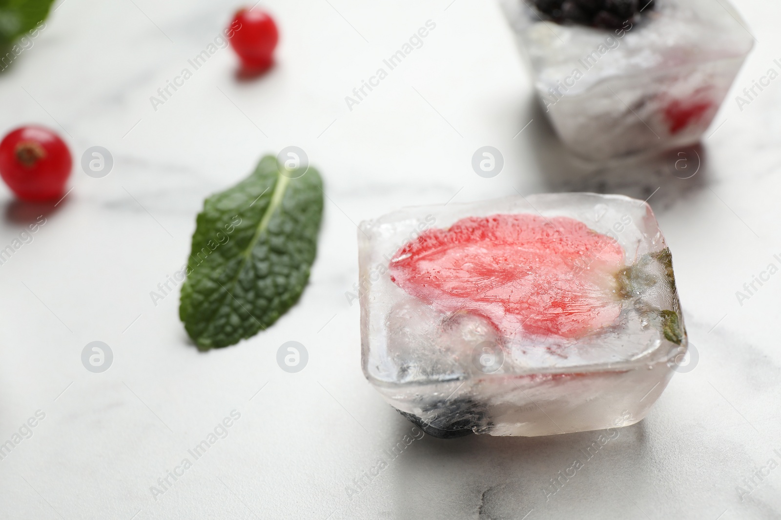 Photo of Ice cube with strawberry on white marble table, closeup