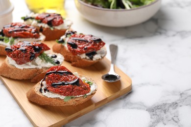 Delicious bruschettas with sun-dried tomatoes, cream cheese and balsamic vinegar on white marble table, closeup. Space for text