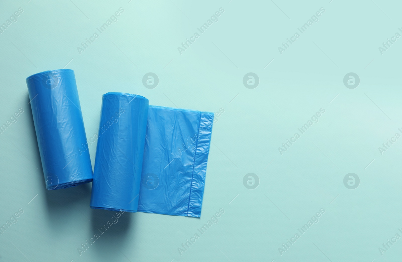 Photo of Rolls of turquoise garbage bags on light blue background, flat lay. Space for text