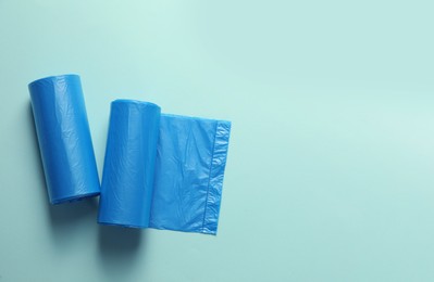 Photo of Rolls of turquoise garbage bags on light blue background, flat lay. Space for text