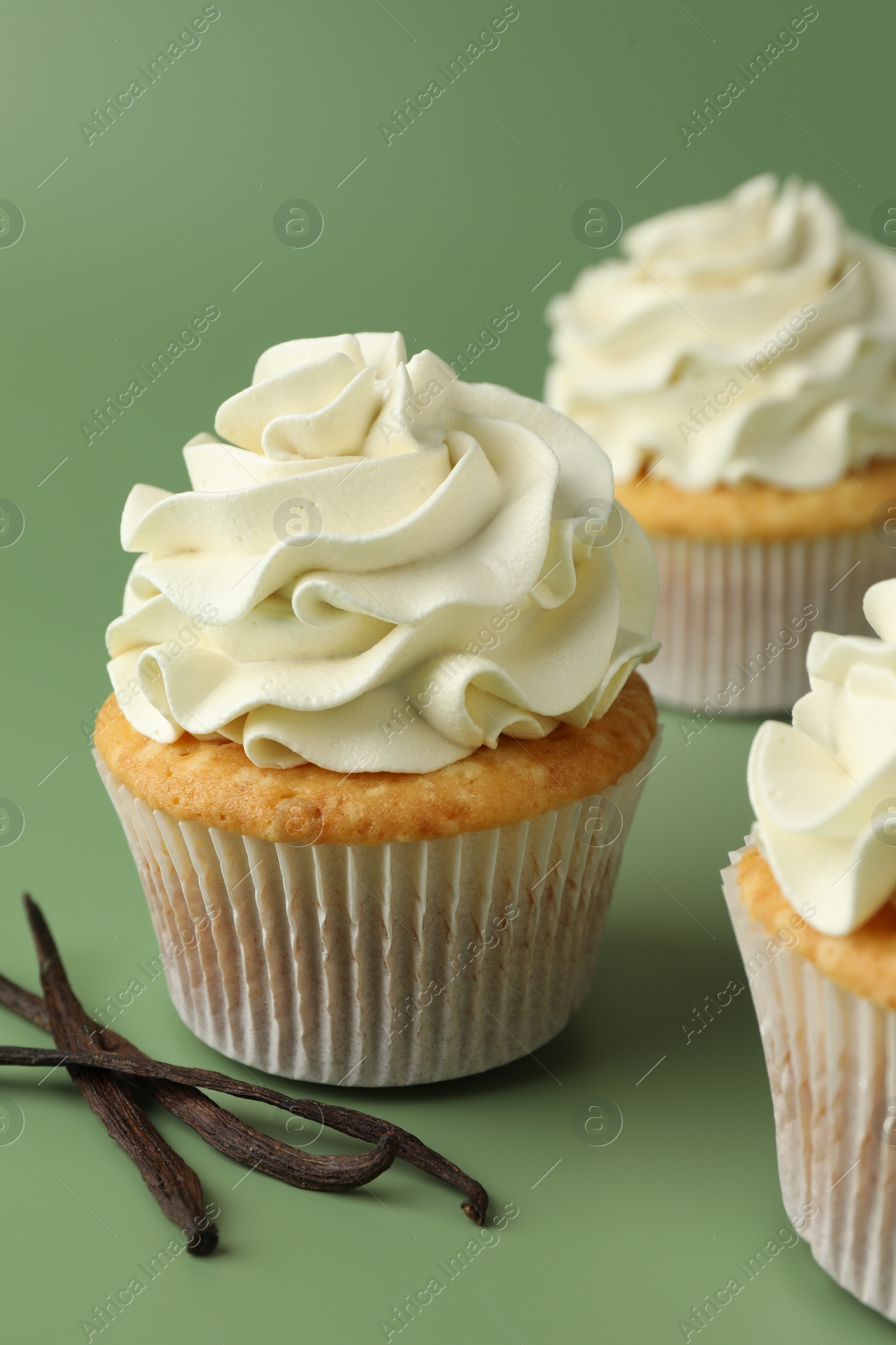 Photo of Tasty cupcakes with cream and vanilla pods on green background, closeup