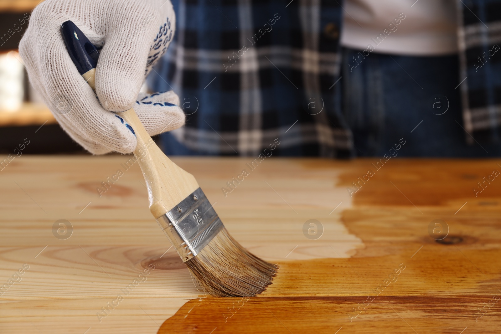 Photo of Man with brush applying wood stain onto wooden surface indoors, closeup