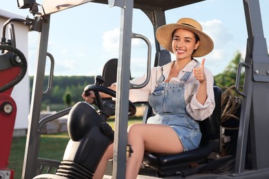 Photo of Smiling farmer driving loader and showing thumb up outdoors