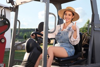 Smiling farmer driving loader and showing thumb up outdoors