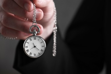 Man holding chain with elegant pocket watch on blurred background, closeup