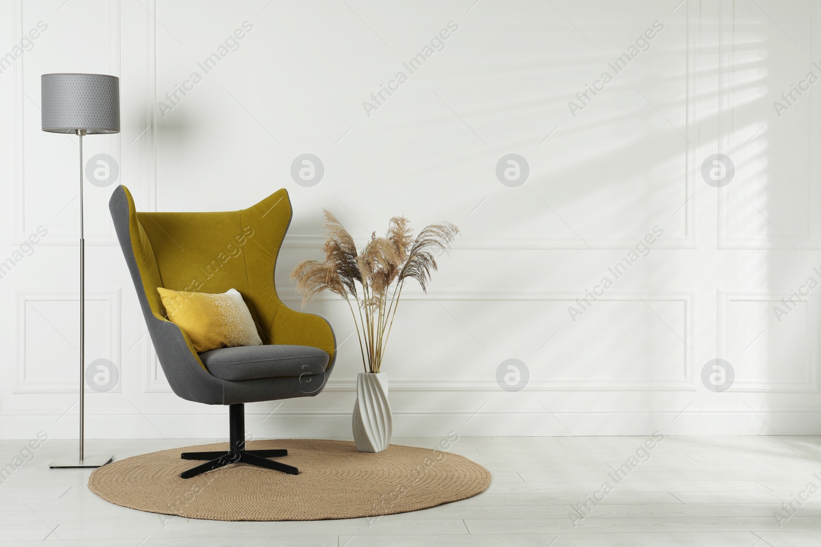 Photo of Stylish interior with armchair and floor lamp near white wall in room, space for text