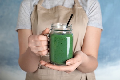 Woman holding mason jar with spirulina smoothie on color background, closeup
