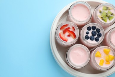 Photo of Tasty yogurt in glass jars and ingredients on light blue background, flat lay. Space for text