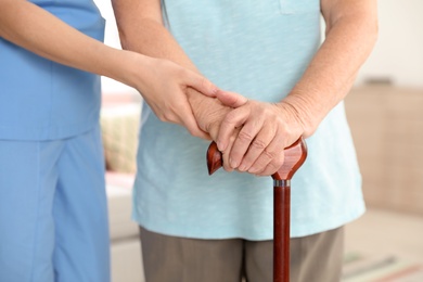 Photo of Nurse assisting elderly woman with cane indoors, closeup