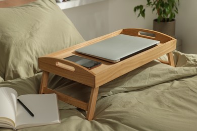 Photo of Wooden tray with modern laptop and smartphone on bed indoors