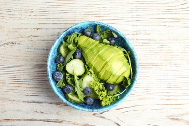 Delicious avocado salad with blueberries in bowl on white wooden table, top view