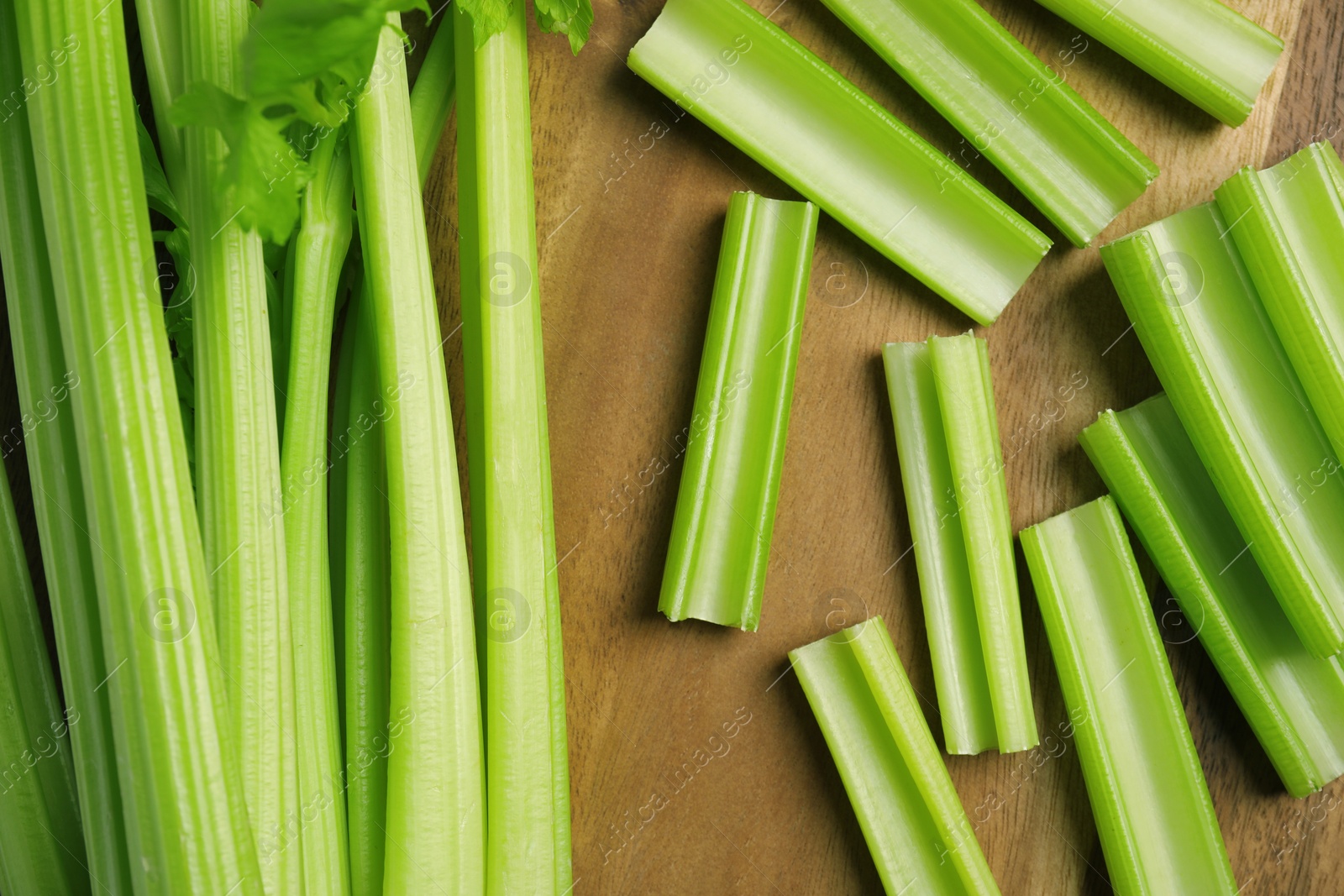 Photo of Fresh cut celery stalks and bunch on wooden table, flat lay