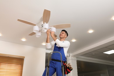 Photo of Electrician changing light bulb in ceiling fan indoors