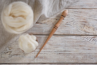 Photo of Soft wool and spindle on white wooden table, flat lay. Space for text