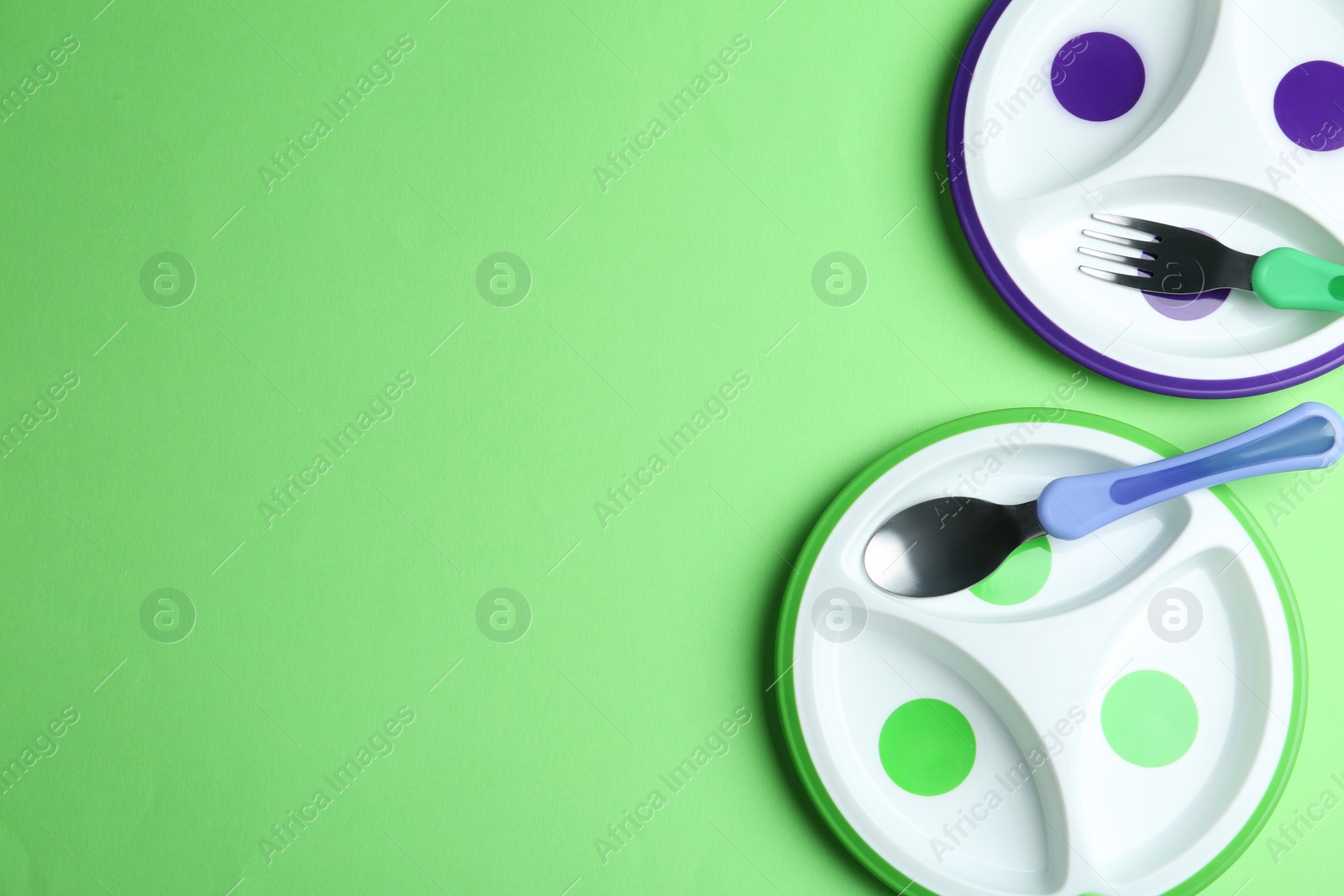 Photo of Plastic section plates and cutlery on green background, flat lay with space for text. Serving baby food